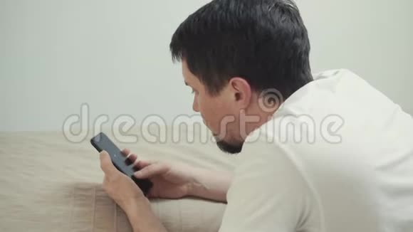 男人在智能手机的触摸屏上滚动页面躺在家里的床上视频的预览图
