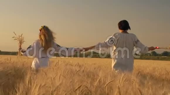 慢动作两个漂亮的女人穿着国家衬衫手里拿着麦穗沿着麦田奔跑握住手视频的预览图