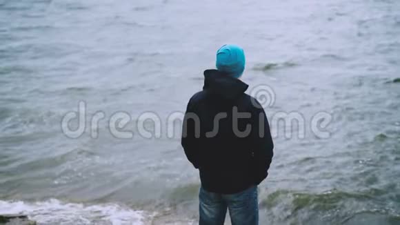 在寒冷的风日站在海边看海浪的年轻人游客的慢动作肖像人民视频的预览图