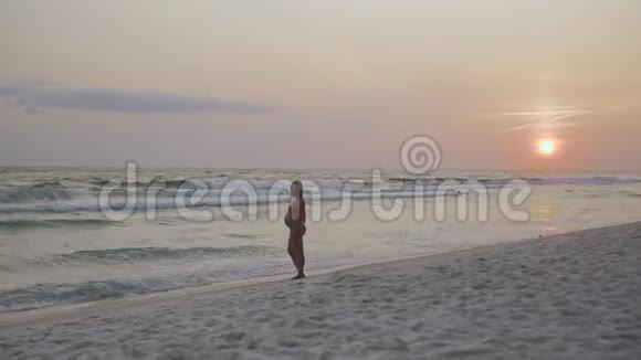 4k日落时在沙滩上沿着海浪散步的时髦孕妇视频的预览图