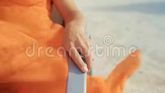 特写镜头女人穿着橙色衣服的手躺在沙滩日光浴的手臂上视频的预览图