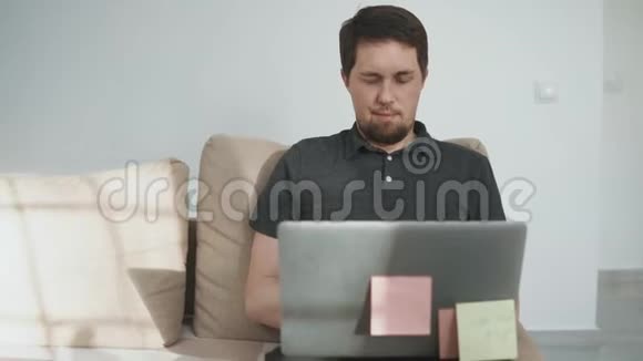 一个长胡子的人正在房间里用笔记本电脑工作坐在沙发上视频的预览图