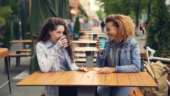 两个年轻的女人在公园里的户外咖啡馆里喝着咖啡和聊天年轻的女人正在玩得很开心视频的预览图