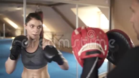 漂亮的女人在健身房和她的教练练习拳击从训练员回来看视频的预览图