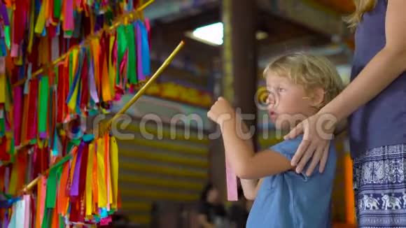 一位年轻的妇女和她的小儿子参观了KekLokSi佛教寺庙并在彩色纺织品上写下了愿望并将其挂在上面视频的预览图