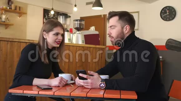 一对年轻快乐的夫妇在咖啡店里休息看着手机屏幕视频的预览图