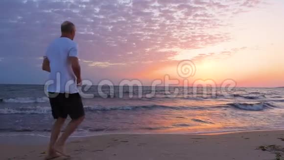 开朗的男人双手高举在海边迎接清晨的日落视频的预览图