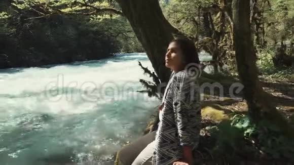 孤独的少年女孩坐在林地的地上看着河溪视频的预览图