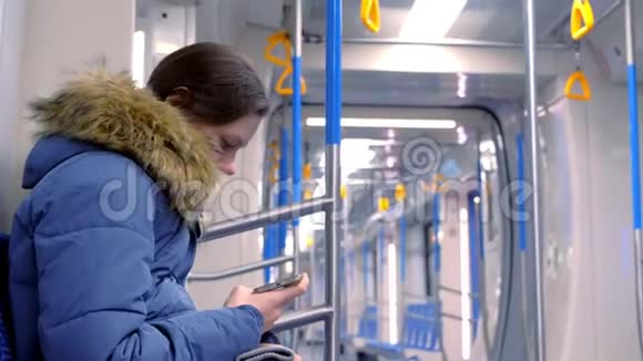 女人坐在一辆空的地铁车里在她的智能手机上看视频侧视视频的预览图