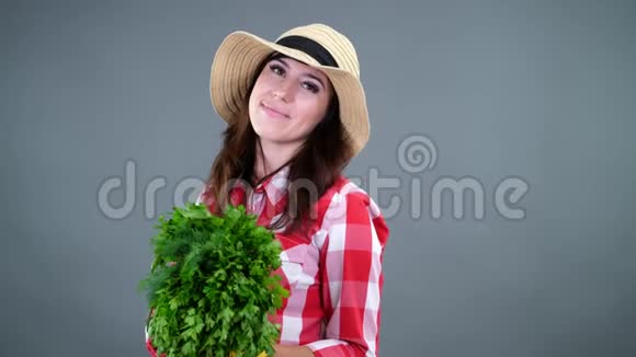 带着格子衬衫手套和帽子的微笑女农民的肖像闻起来有一串新鲜的绿色欧芹和绿色视频的预览图
