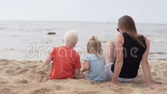 有孩子的女人坐在海滩上视频的预览图