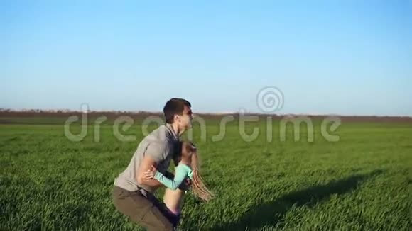 英俊的年轻父亲把他可爱的女儿抛在空中的缓慢动作活跃的生活美丽的绿色田野视频的预览图