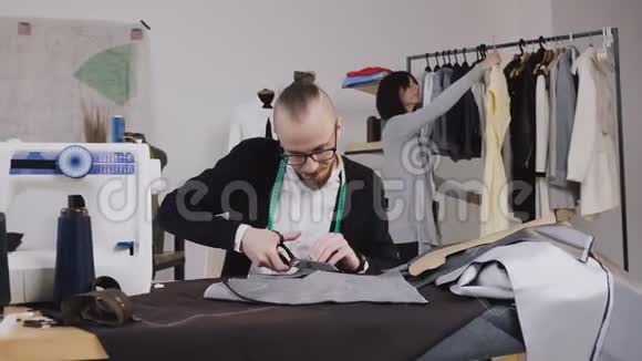 裁缝或时装设计师坐在工作室的工作场所一边用大剪刀或剪刀剪布视频的预览图