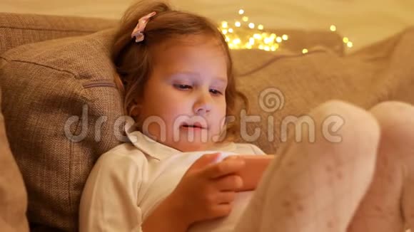 特写肖像儿童女孩在手机屏幕上观看并播放下载的应用程序视频的预览图