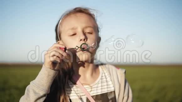 可爱的小女孩在晴天在草地上吹肥皂泡动作缓慢快乐的童年背景模糊视频的预览图