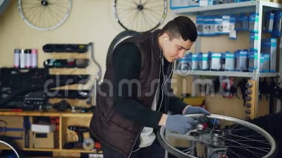 英俊的机械师正在清理自行车车轮的内外轮毂和辐条用一块布听着视频的预览图
