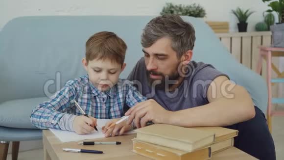 孩子正在学习在练习本上写单词他的父亲正在教他坐在桌子旁解释规则视频的预览图