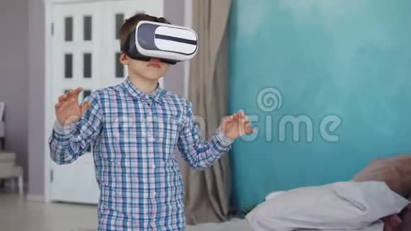 可爱的小男孩正在尝试虚拟现实眼镜站在他的公寓里做手势现代技术视频的预览图
