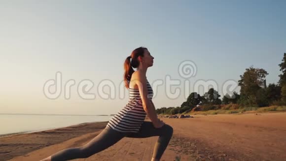 活跃的年轻女性在日落时在海滩上撒布和练习瑜伽视频的预览图