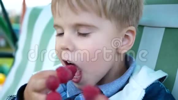 一个可爱的婴儿正在吃红甜多汁的覆盆子那孩子把覆盆子水果放在手指上快乐的童年夏天视频的预览图