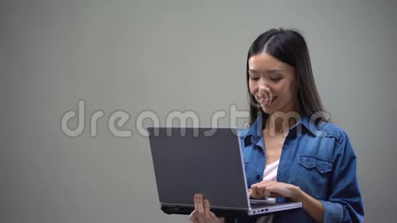年轻的亚洲女性在灰色背景下的笔记本电脑上打字自由职业者视频的预览图