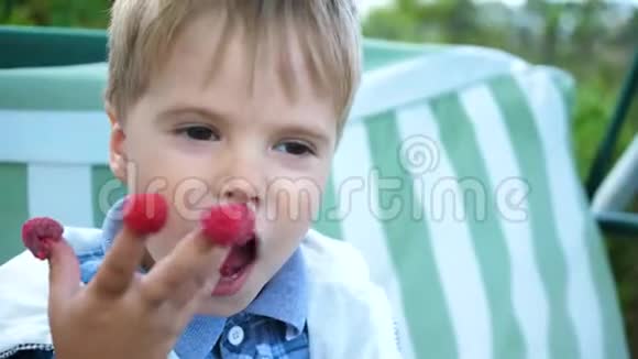 一个可爱的婴儿正在吃红甜多汁的覆盆子那孩子把覆盆子水果放在手指上快乐的童年夏天视频的预览图