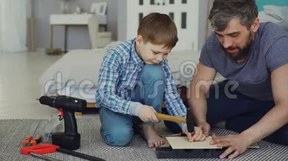 长胡子的父亲和年轻可爱的儿子在家里用木床单做鸟舍儿童和父母的概念视频的预览图