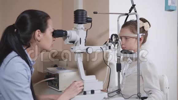 女视镜师在一个医疗办公室检查小女孩的眼睛视频的预览图