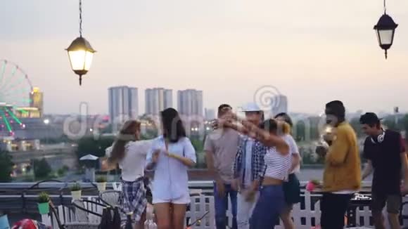 多种族的一群朋友正在屋顶跳舞在夏天的晚上和DJ举行一个凉爽的聚会快乐的青年视频的预览图