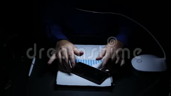 黑暗办公室里的商人在紧张地打手势在桌子上转动手机视频的预览图