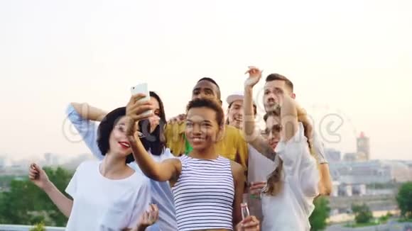 动作缓慢漂亮的非洲裔美国妇女录制屋顶派对视频与她的朋友跳舞和看着视频的预览图