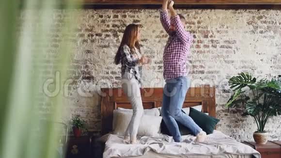 一对年轻美丽可爱的夫妇在家里的床上跳舞玩得很开心笑得很慢粗心空闲时间视频的预览图