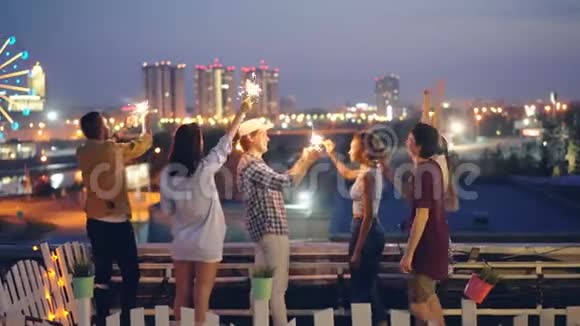 快乐的朋友们正在燃烧孟加拉灯一起站在屋顶上跳舞庆祝节日娱乐视频的预览图