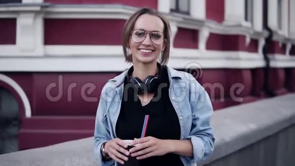 一位戴着眼镜的年轻漂亮女孩的美丽景色她站在背景上带着一座红色的经典建筑微笑着视频的预览图