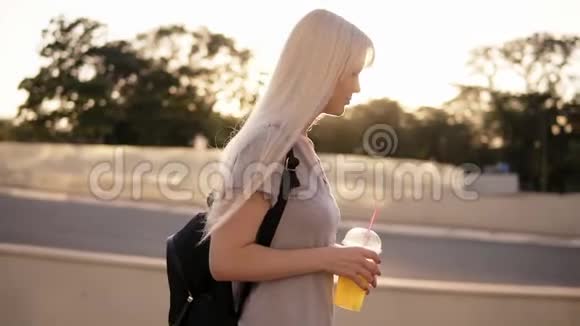 一个美丽的长发女人走在街上带着黑包和一杯柠檬水的轻松女孩慢慢地视频的预览图