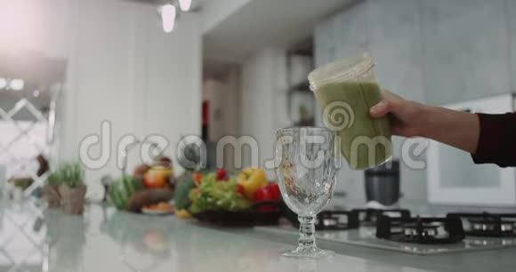 早上厨房里的夫妇在一个大玻璃杯上倒了一块健康的绿色冰沙缓慢的动作视频的预览图