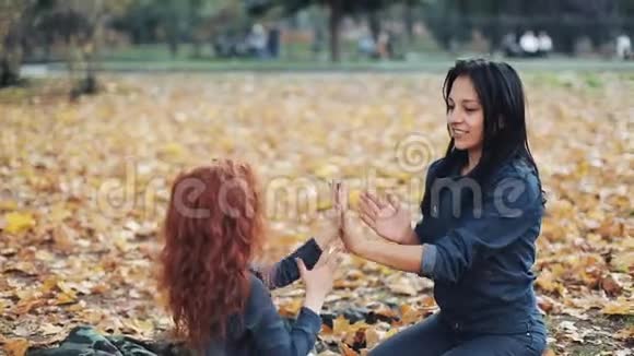 小红发女孩和妈妈一起在秋天公园度过时光他们玩拍手视频的预览图