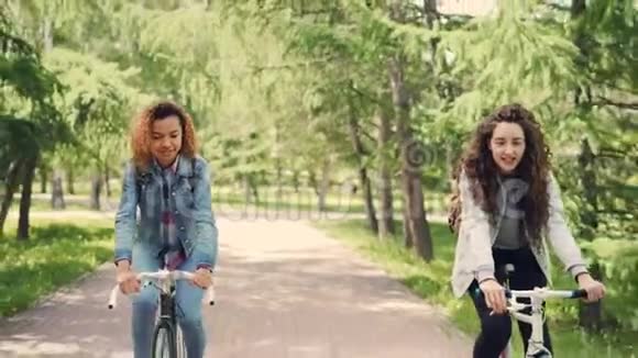 两位快乐的年轻女士正在公园里骑自行车谈论着享受美丽的自然和温暖的晴天积极的生活方式视频的预览图