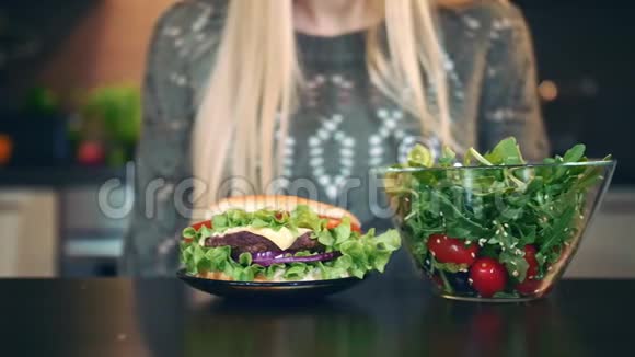 女孩喜欢沙拉而不是汉堡包有魅力的年轻女性选择吃健康沙拉作为晚餐而坐在视频的预览图