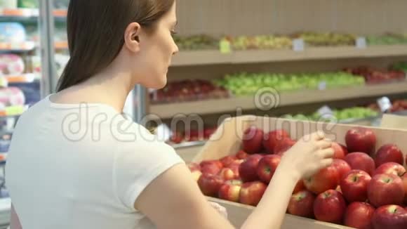 年轻女子在杂货店买健康食品素食女孩选择新鲜的红苹果视频的预览图