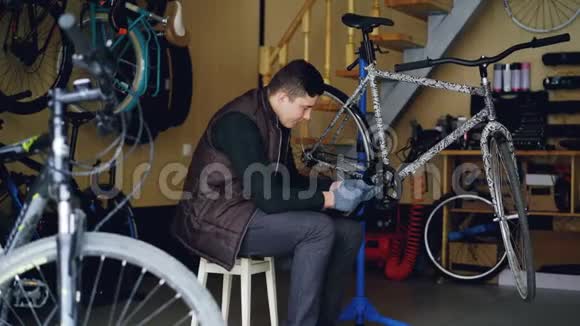多莉拍摄的焦点年轻的机器修理破碎的自行车踏板坐在凳子附近的现代自行车在工作场所视频的预览图