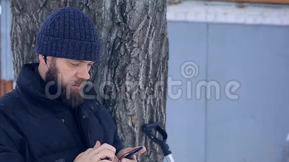 冬天可怜的胡子男通过电话用耳机听音乐视频的预览图