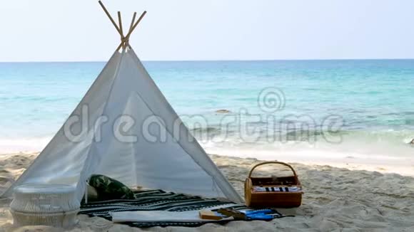 4K浪漫的白色野餐帐篷白色沙滩上有篮子食物背景是清澈的水和蓝天视频的预览图