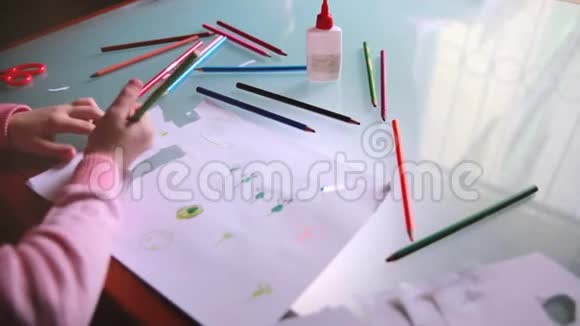 俯视镜头左滑动的小白种人女孩在纸上用各种颜色的铅笔在一张桌子上视频的预览图
