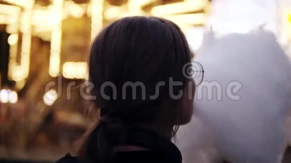 一个女孩在游乐园散步吃棉花糖的背面景色穿着透明衣服的金发短女视频的预览图
