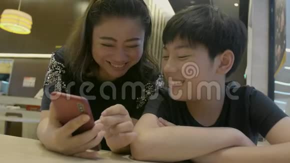 4慢动作的快乐亚洲男孩和他的妈妈看着智能手机带着微笑的脸视频的预览图