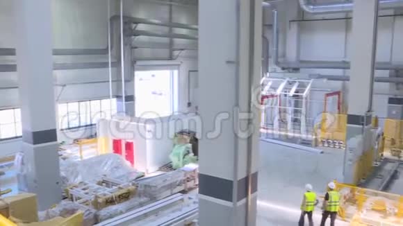 在一个大型制造部门和两名穿黄色夹克和安全帽的男性工人的空中视野场景视频的预览图