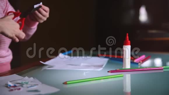镜头滑落在穿着粉色毛衣的小女孩的手上她在桌子上用各种文具剪出纸的形状视频的预览图