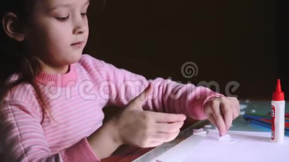 一个美丽的学龄前欧洲小女孩的特写镜头她穿着粉红色的毛衣坐在桌子旁粘着纸的形状视频的预览图