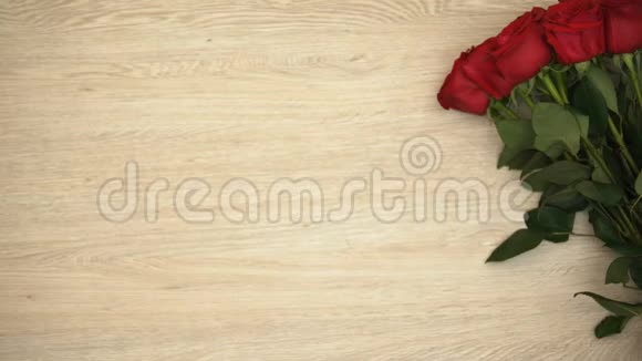 男性将红色礼品盒放在靠近玫瑰花束的木桌上模板视频的预览图